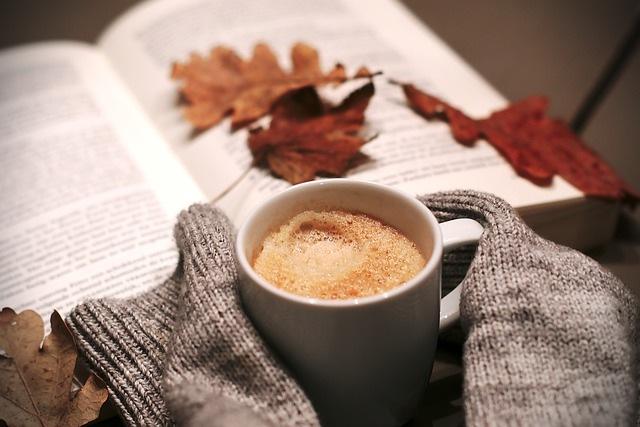 Kaffeetasse mit Kaffee und einem aufgeschlagenen Buch im Hintergrund